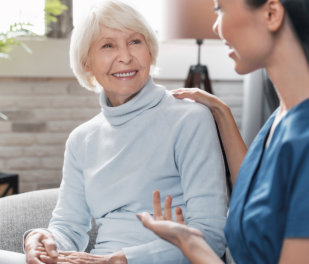 Caregiver smiling and talking to aged woman while taking care of her at home