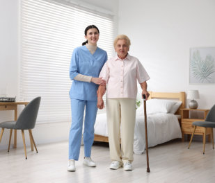 Nurse assisting senior woman with walking cane indoors