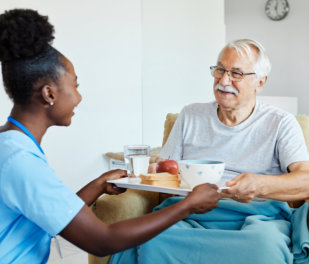 Doctor or nurse caregiver serving a meal to senior man